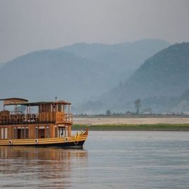 MV Rudra Singha Hausboot auf dem Brahmaputra mit blauschimmernden Bergen am Horizont
